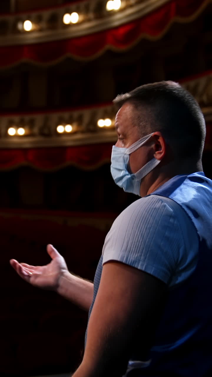 Actor on stage. Man in medical mask is talking to empty auditorium. Speaker in protective mask during the rehearsal. Rear view. Vertical video