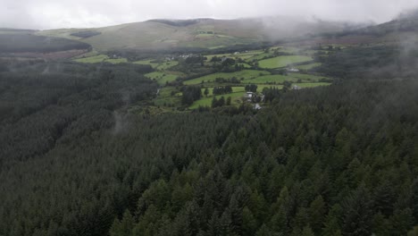 drone shot of a green mountain valley in ireland with fields, a forest and low lying clouds