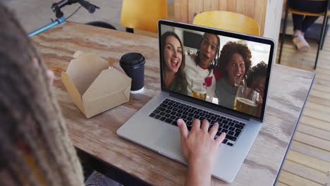 mujer tomando un bocadillo mientras hace una videollamada en una computadora portátil en una cafetería