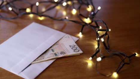 polish zloty cash in an envelope as a christmas gift, lying next to the christmas lights on the table