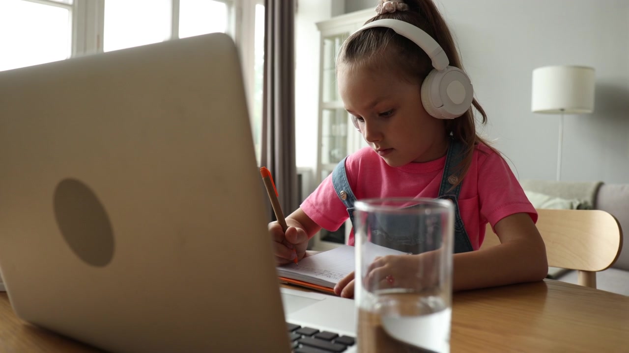 Little Girl Learning Online and Writing in Notebook