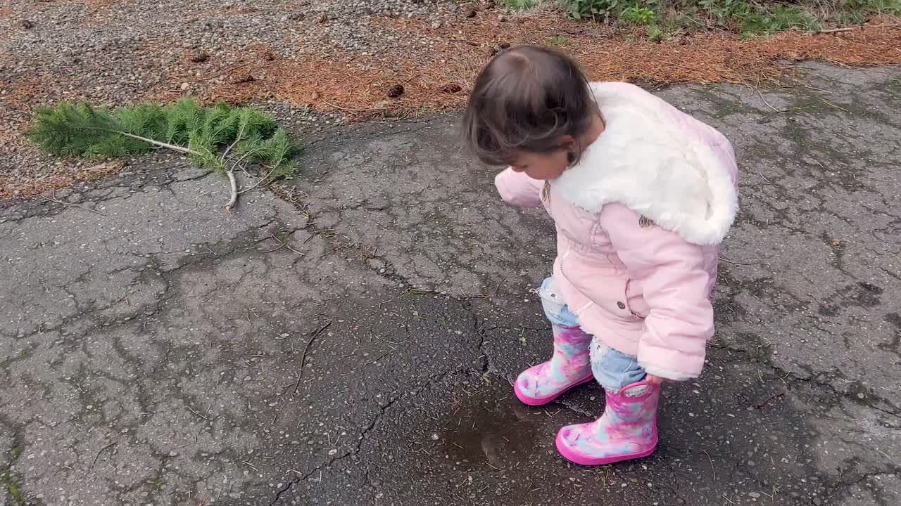A cute little girl jumping in a puddle then running away wearing pink rubber boots