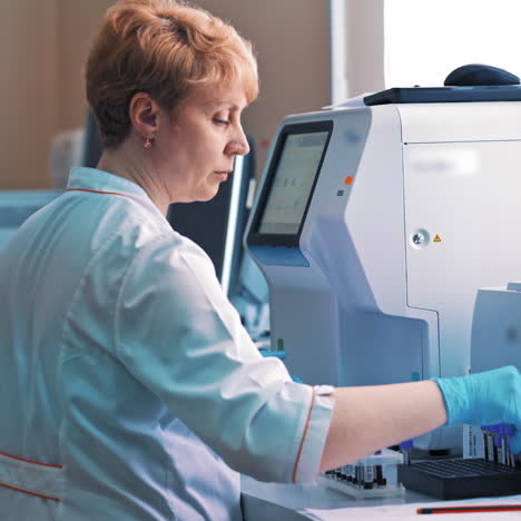 professional laboratory technician is holding a vial near the automated medical machine. woman scientist is working in a modern pharmaceutical laboratory.