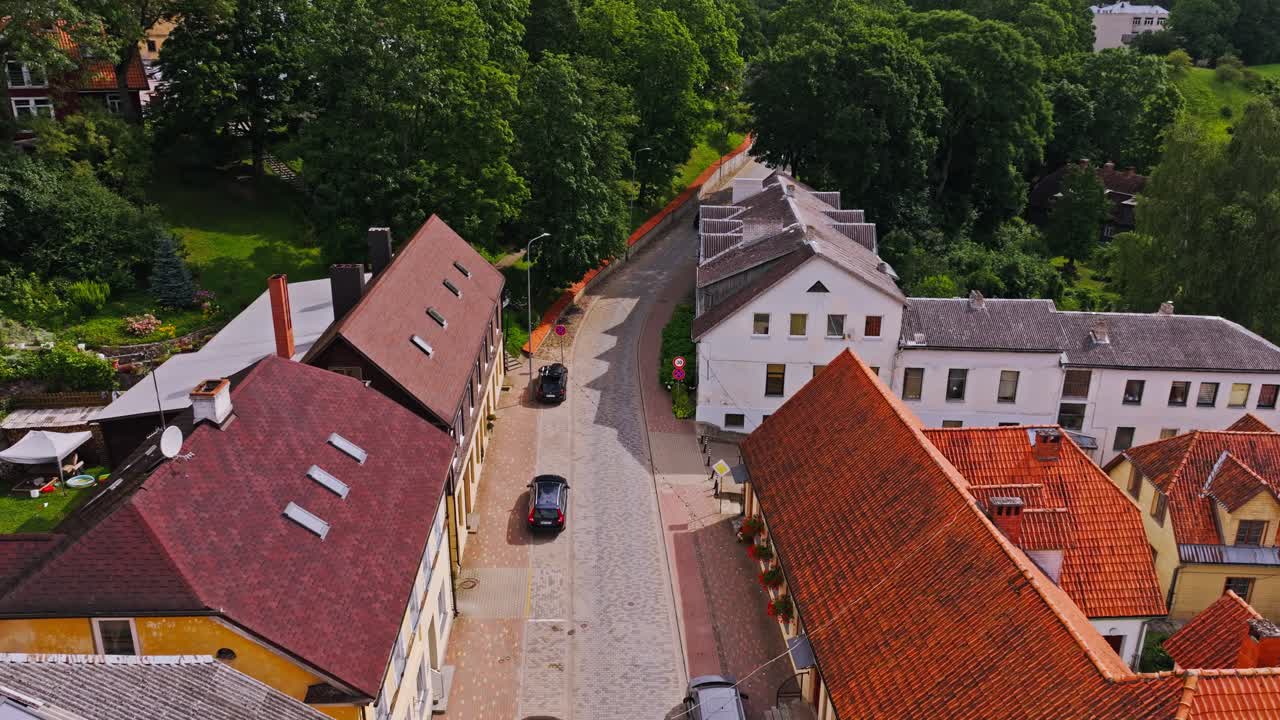 Drone glides above old town street near lake, as lone car moves through frame
