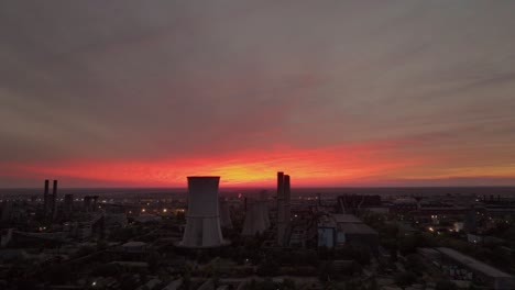 tracking drone shot showing smokestacks against a vibrant orange-clouded sunset, offering a striking industrial landscape