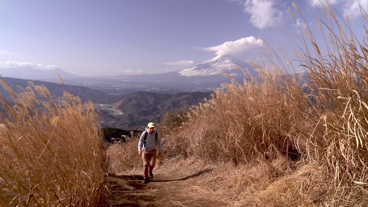 excursionista masculino caminando por el camino entre la hierba amarilla alta con el monte fuji como telón de fondo