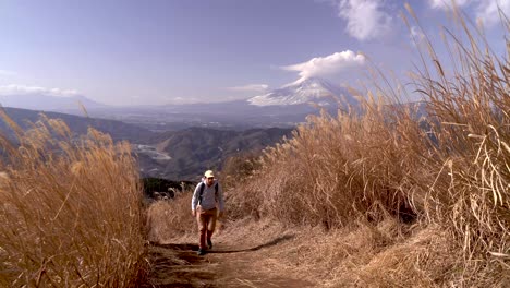 male hiker walking up path in between high yellow grass with mount fuji in backdrop