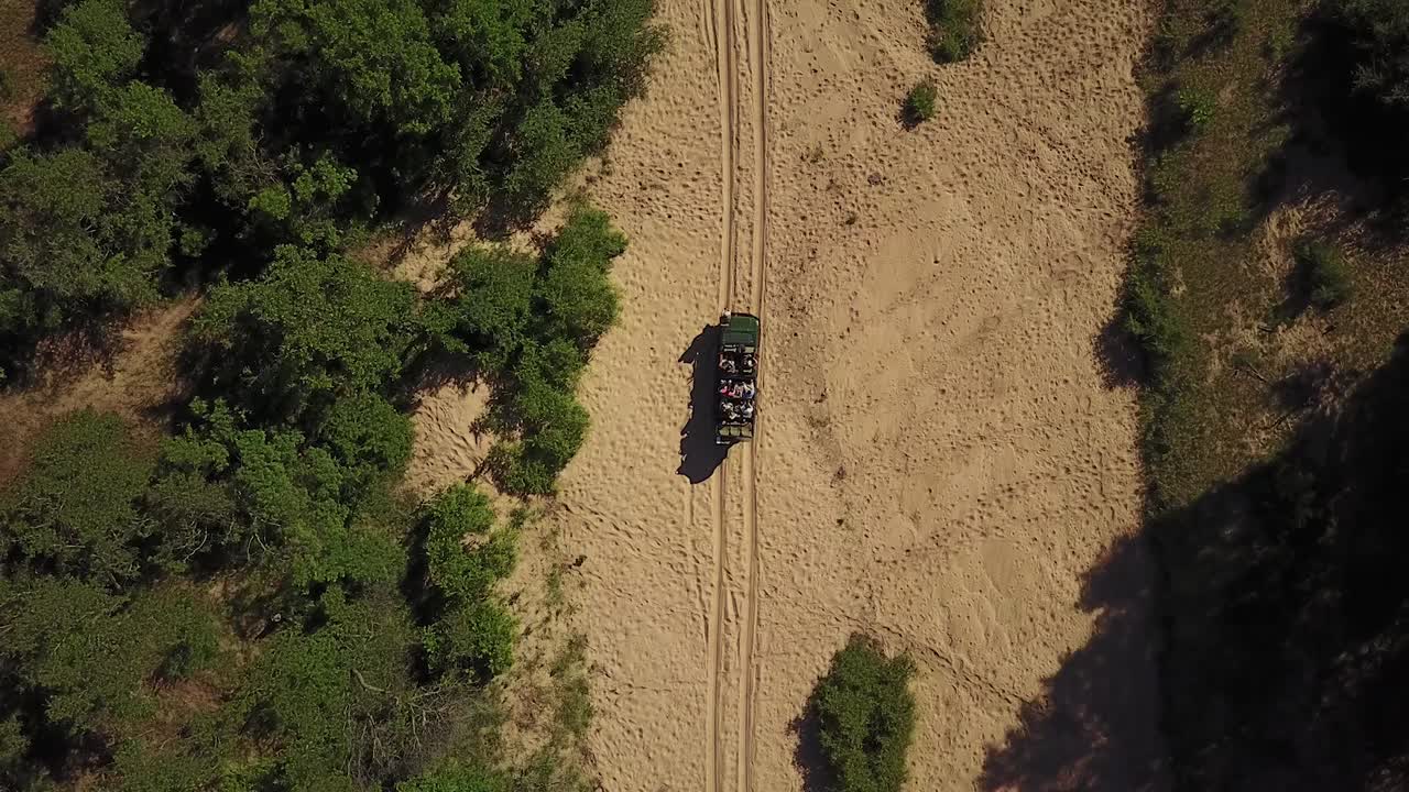 Ripresa aerea con drone di veicoli da safari in un letto di fiume prosciugato, sotto il caldo sole africano pomeridiano.