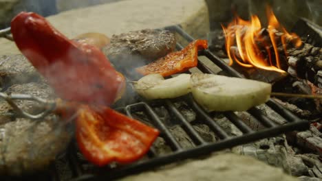 tongs flip a red pepper over on a smoking grill