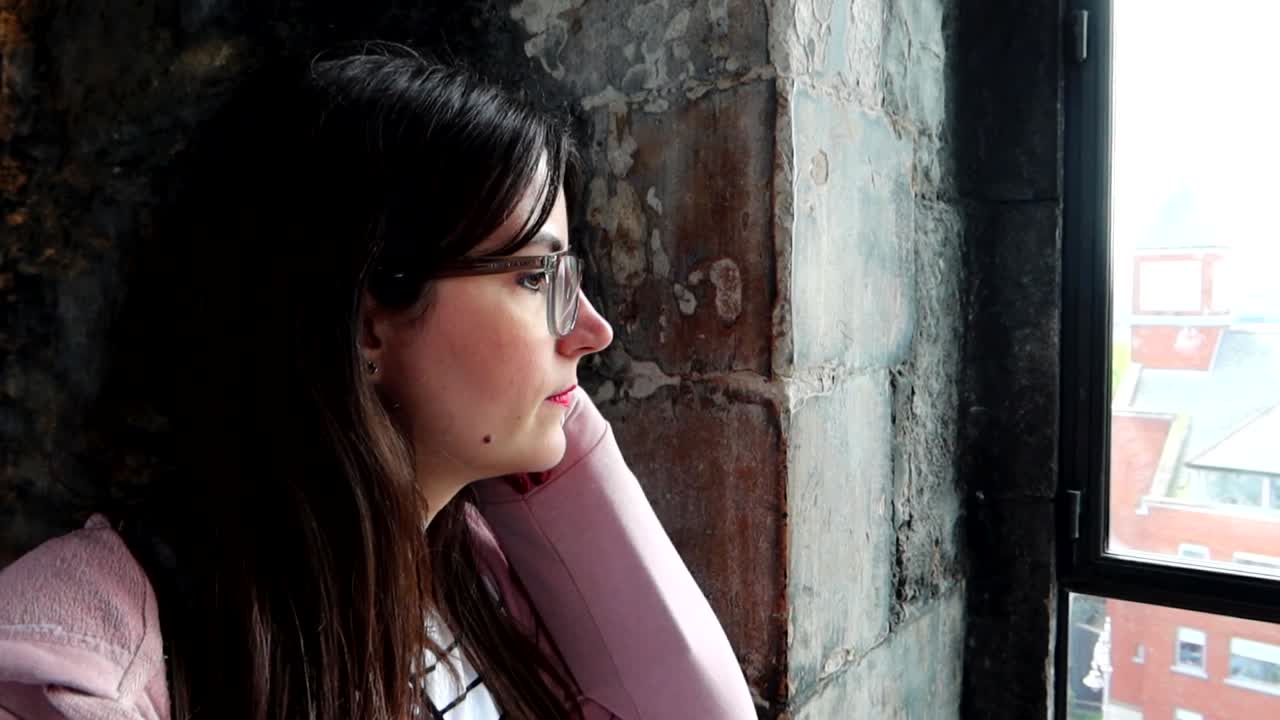Giovane donna pensierosa che guarda attraverso una finestra all'interno di un vecchio edificio urbano