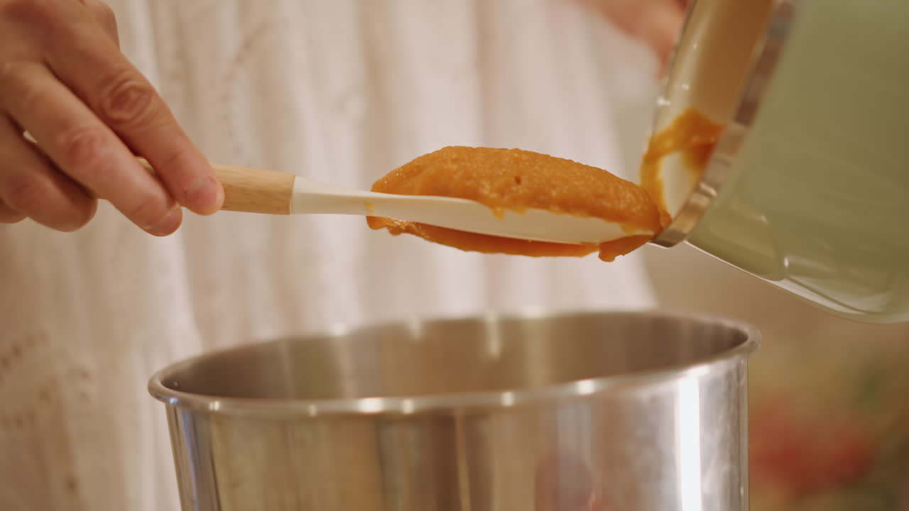 Versare con attenzione la zucca in una ciotola. Pentolame vintage usato per versare e raschiare il composto di zucca. Primo piano di una scena di cottura tradizionale con purea di zucca versata e raschiata accuratamente.