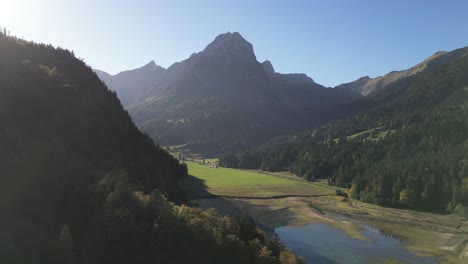 Toma-Aérea-De-Los-Alpes-Suizos-Y-Un-Lago-Situado-En-El-Valle-Cerca-Del-Bosque.