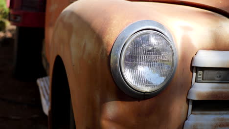 slide left along the front of an old rusty vintage truck fender with glass headlight and grill in the sunlight