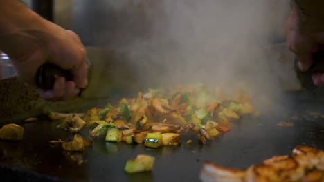 chef sautes and flips mixed vegetables on hibachi grill top, close up slow motion 4k