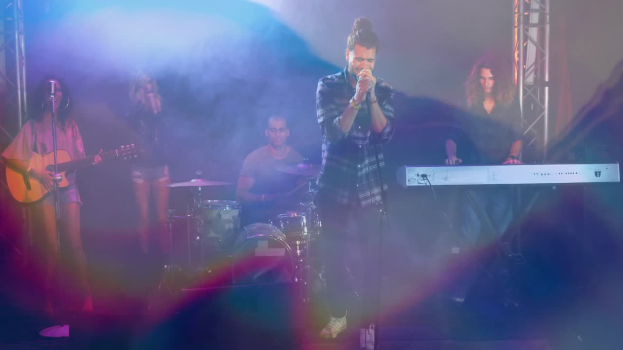 무대에서 연주하는 밴드와 함께 노래하는 백인 남성 위에 반 ⁇ 이는 파란 빛의 애니메이션