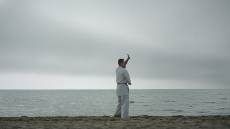 Fit-man-workouting-karate-technique-on-beach.-Fighter-training-combat-skills.