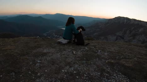 niña sentada y abrazando a un perro labrador negro en una montaña