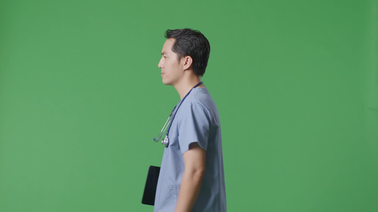 Side View Of Asian Male Doctor With Stethoscope Holding A Tablet While Walking On Green Screen Background In The Hospital