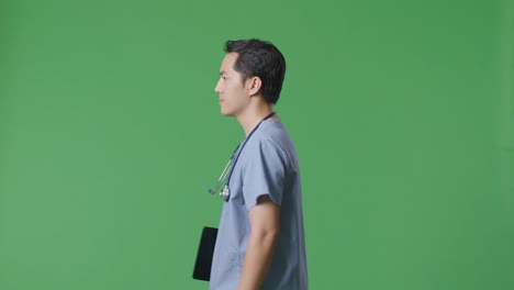 side view of asian male doctor with stethoscope holding a tablet while walking on green screen background in the hospital