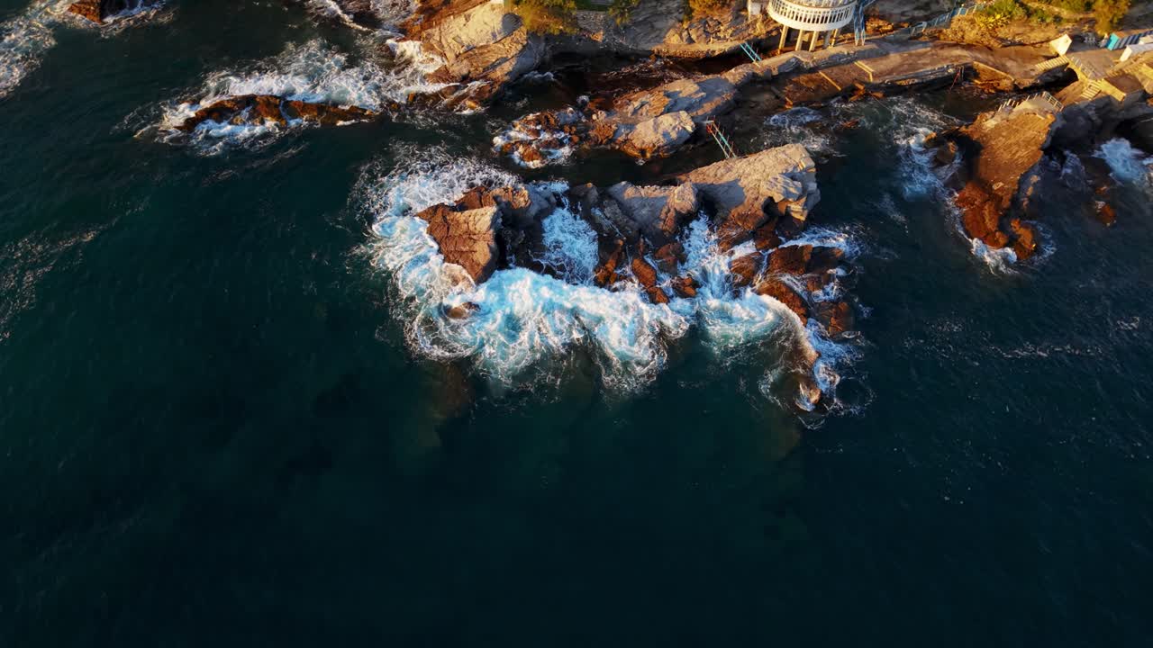 Rocky coastline of Genoa, Italy, with waves crashing against the shore at sunset