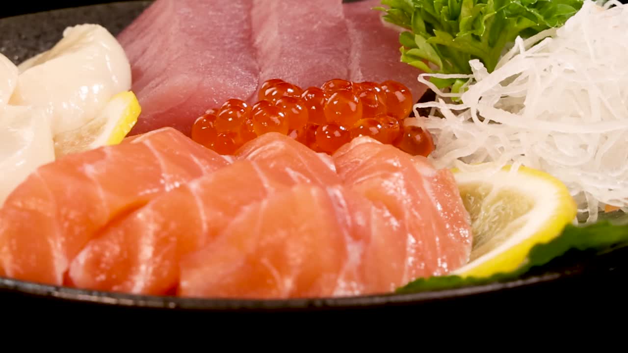 Una macro dettagliata di salmone, tonno, capesante e ikura in rotazione su sfondo nero