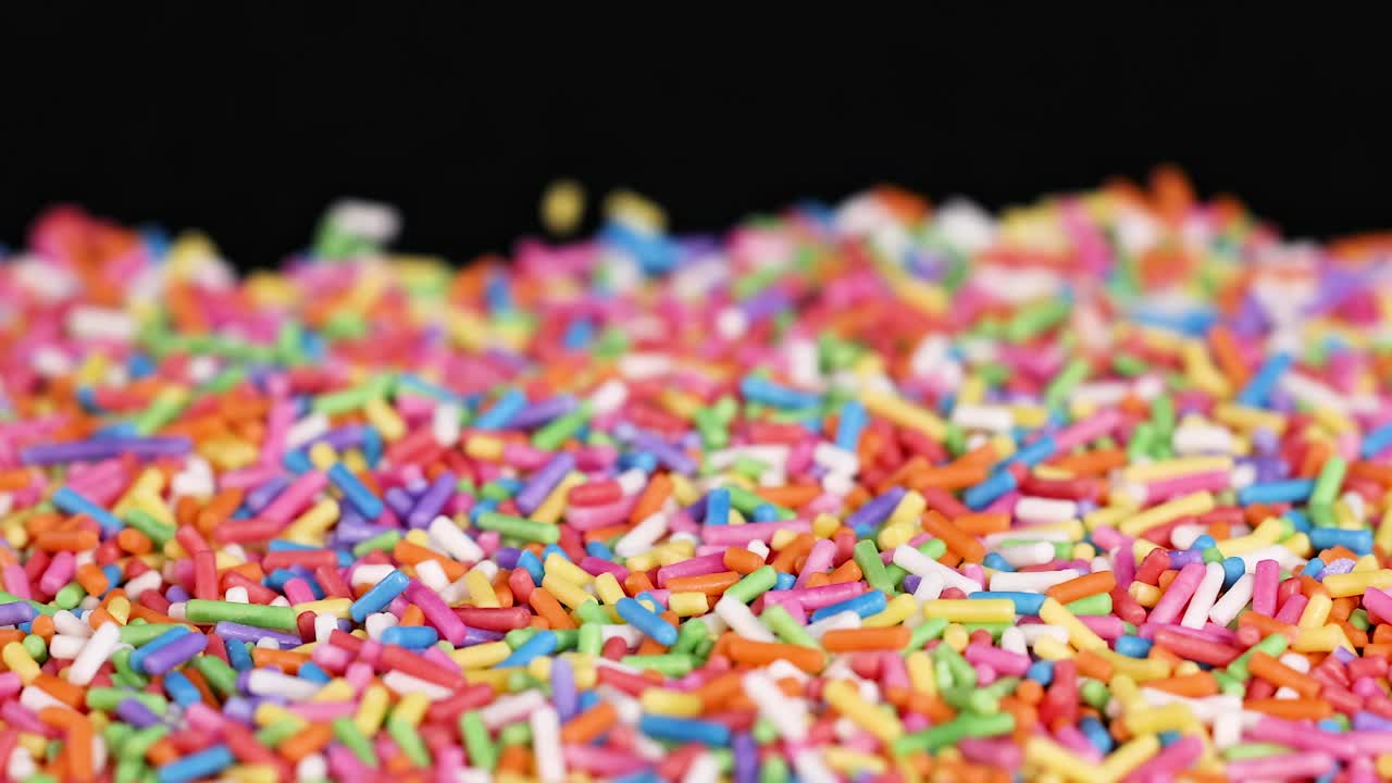A close-up view of multicolored sprinkles creating a vibrant, textured surface against a dark background.
