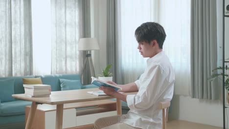 side view of asian man student reading a book while studying at home