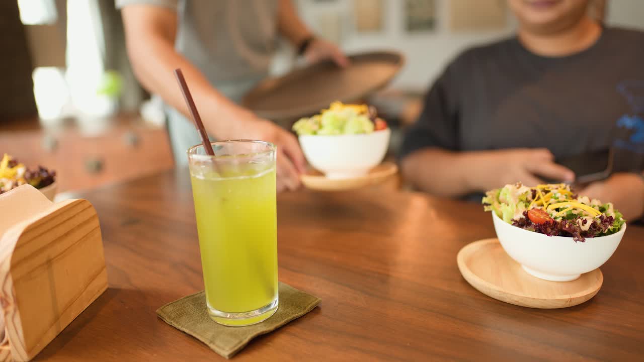 Server places salad bowl beside green tea for customer in sunlit, casual cafe setting