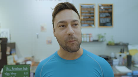 hombre alegre de unos 30 años comiendo ensalada fresca sonriendo mirando a la cámara dentro de un pequeño café