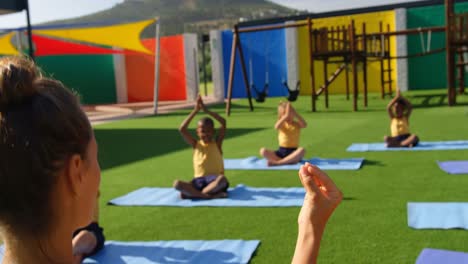 Vista-Trasera-De-Una-Maestra-Enseñando-A-Los-Escolares-A-Realizar-Yoga-En-El-Patio-De-La-Escuela-4k