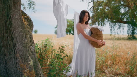 young woman holding laundry basket walking dry grass garden. girl stepping field