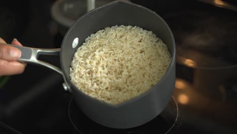 close up of boiling water on n electric stove to cook raw whole grain rice in a medium saucepan
