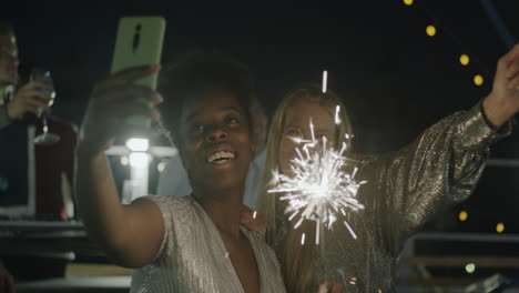 two friends taking a selfie with sparklers at a rooftop party