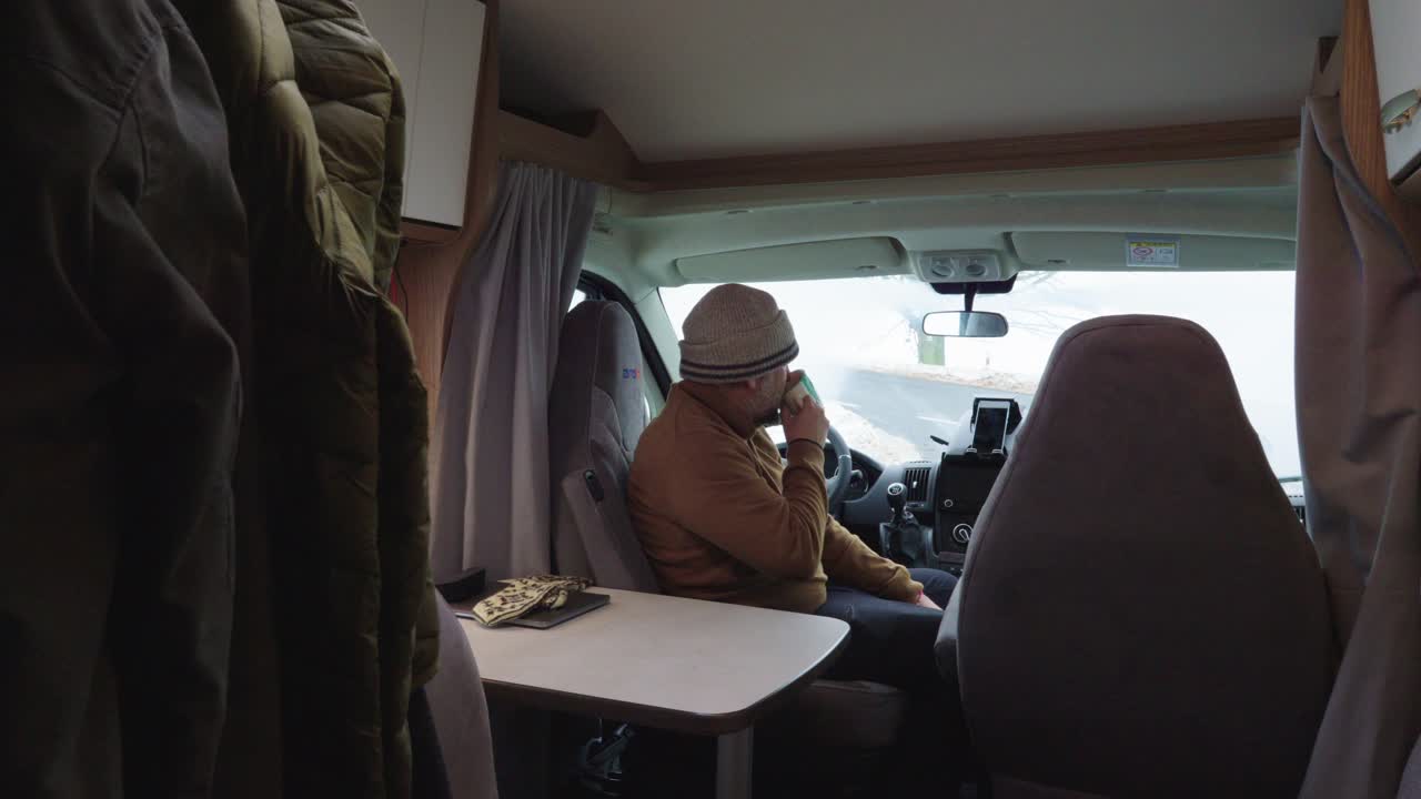 Uomo seduto in camper che beve una tazza di caffè o tè, vista interna grandangolare