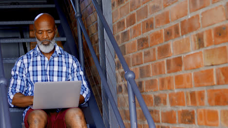 Senior-man-using-laptop-on-stairs-in-living-room-4k