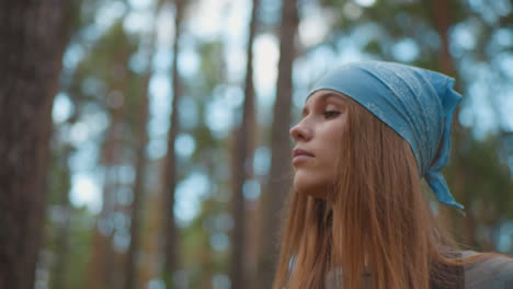 lady hiking through a vibrant forest, looking down contemplatively, wearing a blue bandana and backpack, surrounded by tall trees and lush greenery with warm light filtering through leaves