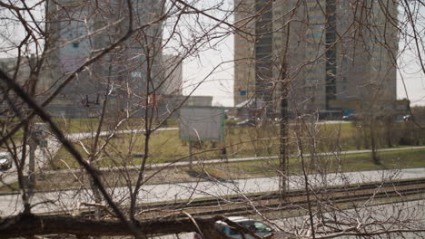 close view of an urban scene featuring traffic, leafless trees, and high-rise buildings, the branches create a natural frame