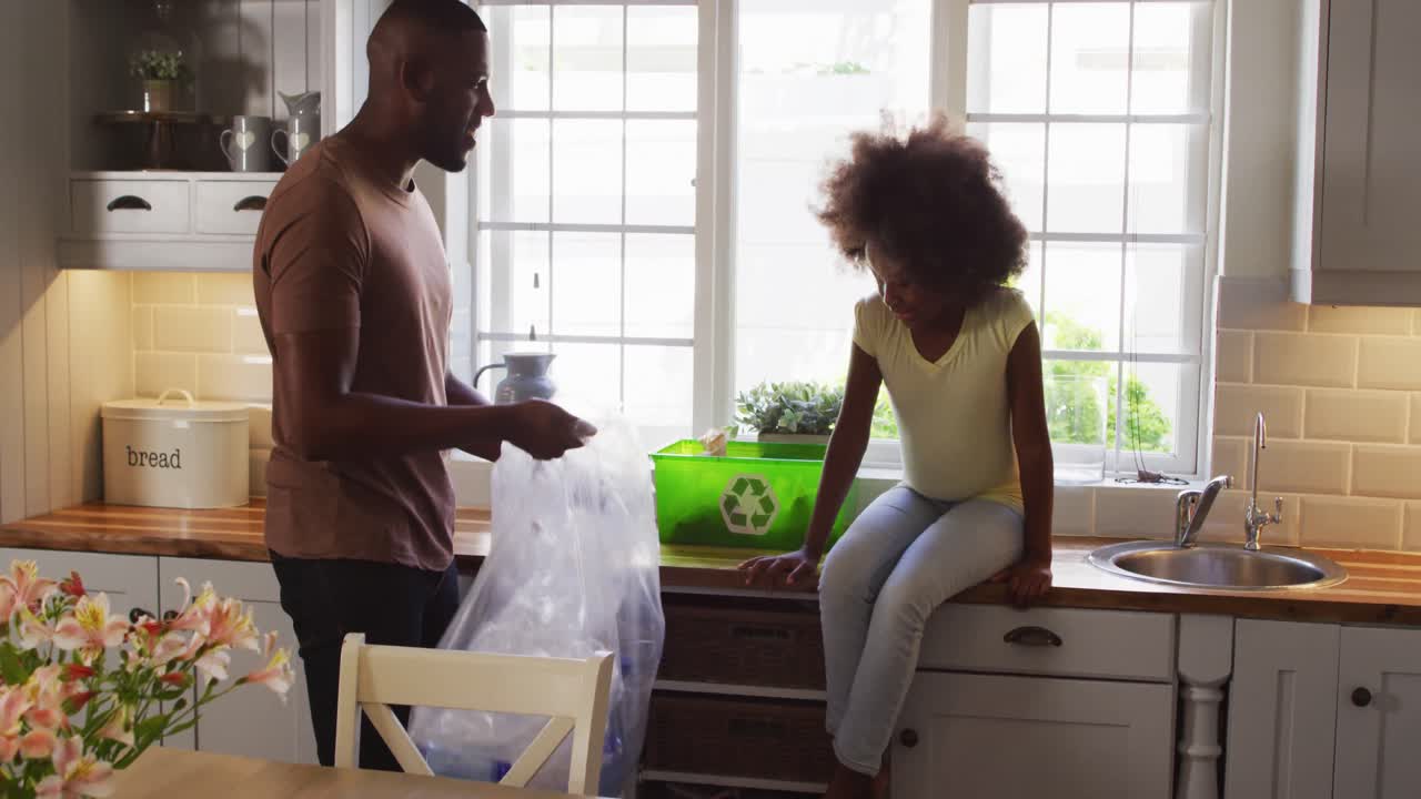 African american daughter and her father sorting recycling and high fiving in kitchen
