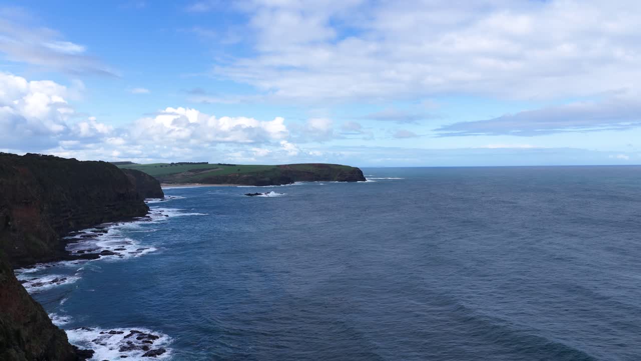 Drone camera pans revealing dramatic rocky coastline, ocean waves, and cloudy sky at Cape Schanck