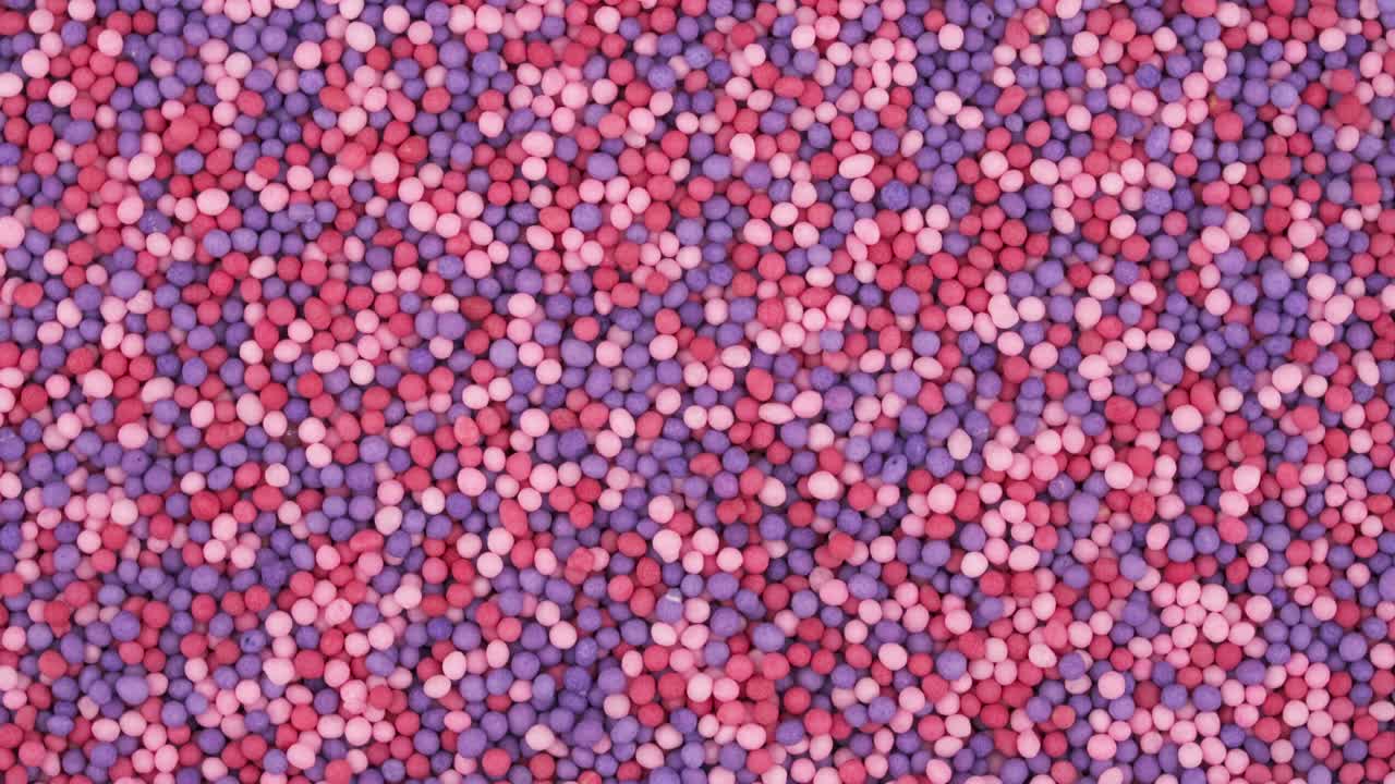 Top view from above of small red, rose and blue sprinkles sugar candies rotating.