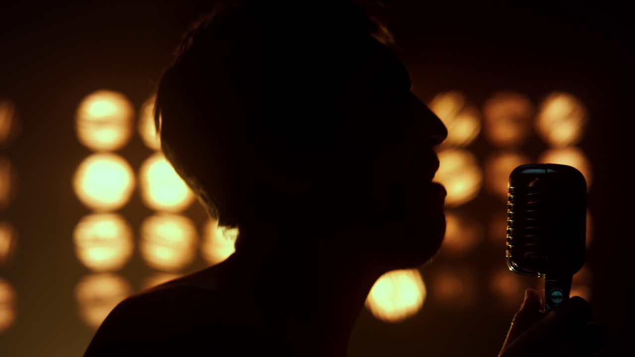 Silhouette di un ragazzo che canta una canzone in un nightclub, primo piano. Vocalist sconosciuto che canta.