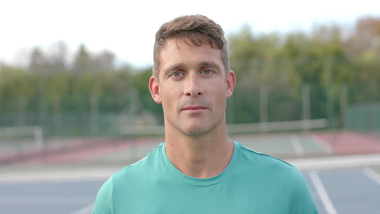 retrato de un feliz jugador de tenis caucásico sosteniendo una raqueta y una pelota en una cancha al aire libre, en cámara lenta