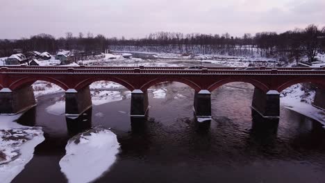 aerial view of old red brick bridge across the venta river in kuldiga, latvia in overcast winter day, venta rapids in background, wide angle drone shot moving backwards