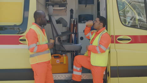 latin and afroamerican medical assistances drinking coffee and talking outside the ambulance