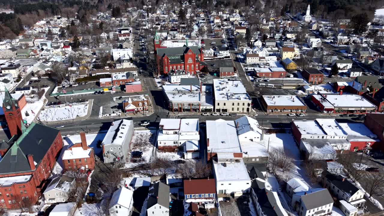 Ware, Massachusetts şehir merkezinin kışın havadan görünümü; karla kaplı çatılar, tarihi tuğla kilise ve parlak güneş ışığı altındaki küçük kasaba sokakları. Geniş açı çekim.