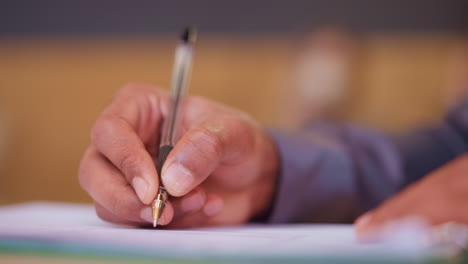 close-up hand gripping pen while writing on paper, detailed focus on motion and pen tip, individual engaged in office task or academic work, warm blurred background suggests calm, productive atmosphere