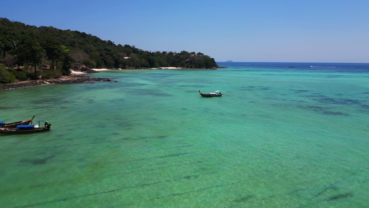 Aerial view of a tropical island beach with turquoise water showing long tail boats waiting for tourists in thailand