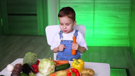 kid chopping veggies in bright kitchen. a young child sits at a table with various fresh vegetables, focused on holding a carrot in a colorful kitchen