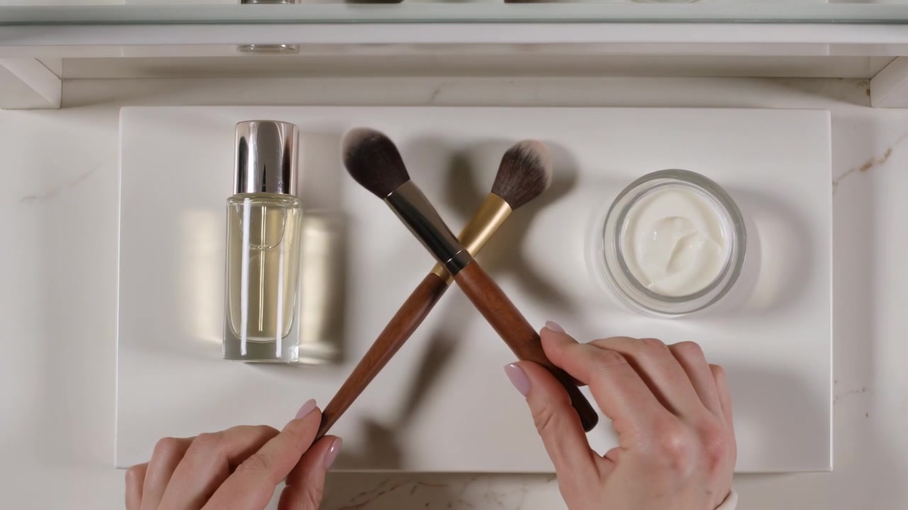 Entering hands wearing cuffs placing pump, cream at vanity, dipping brushes, forming X for demo