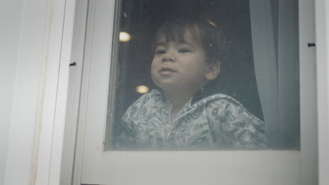 a happy two-year-old kid looks out the window, laughs happily